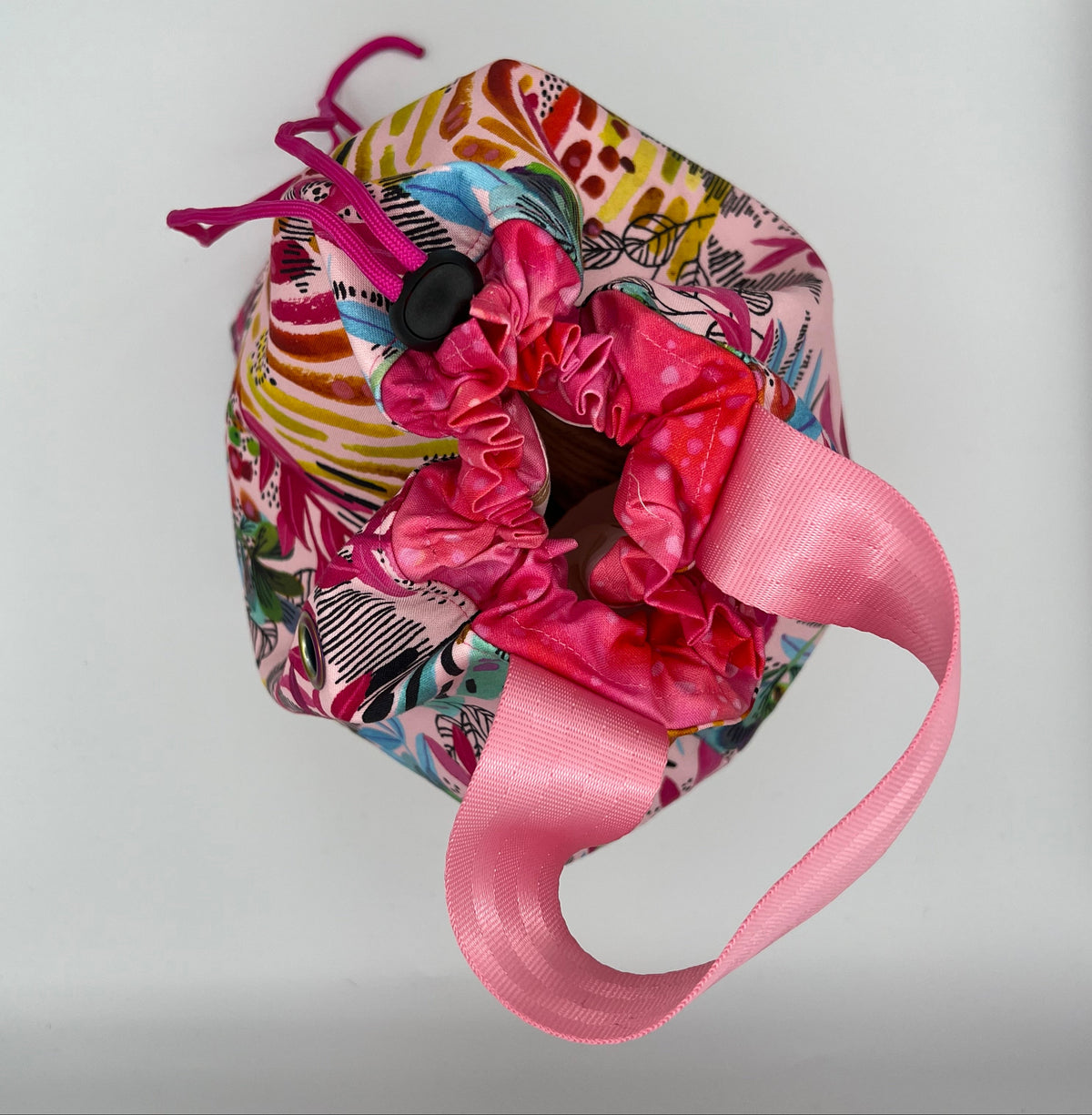 A drawstring tote with a colorful abstract patterned fabric body, a bright pink closure, and a pink handle, photographed against a plain light background.