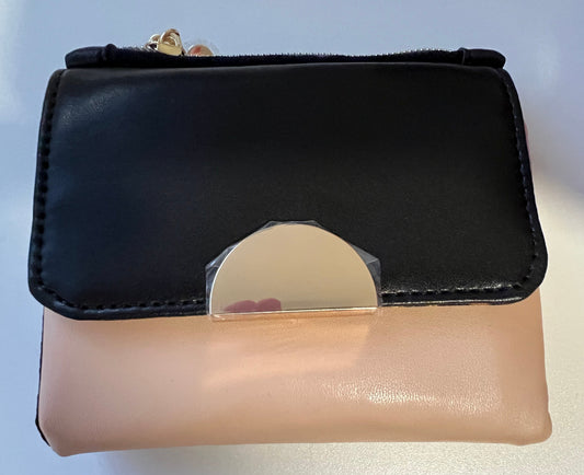 A small zip-around wallet with a black front flap and a blush pink body, featuring a large metallic gold semicircle clasp and a gold zipper pull.