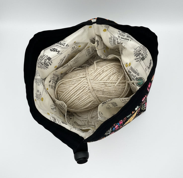Interior view of drawstring tote bag with a cream lettered interior and skein of yarn, set against a plain light gray background.