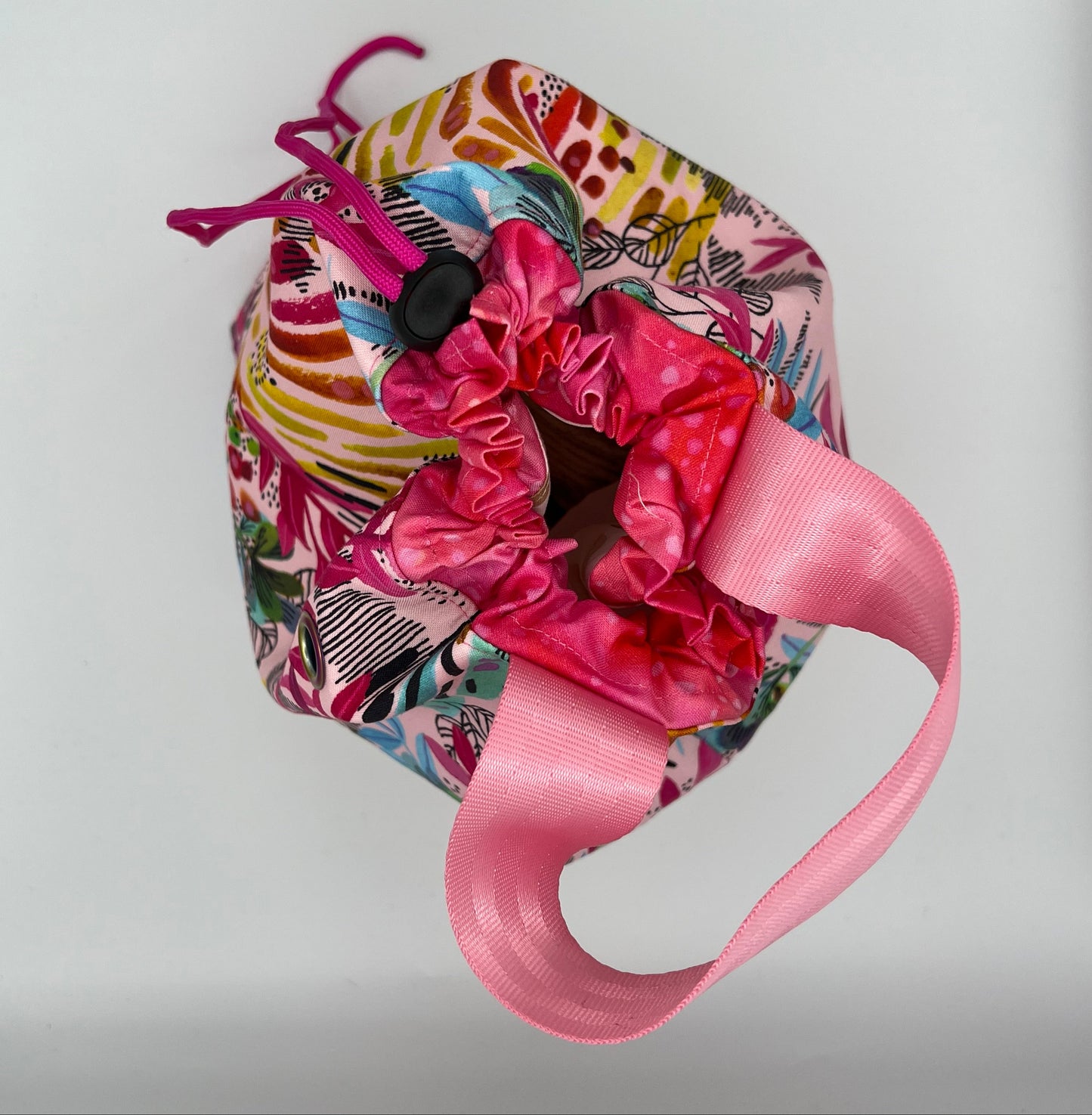 A drawstring tote with a colorful abstract patterned fabric body, a bright pink closure, and a pink handle, photographed against a plain light background.