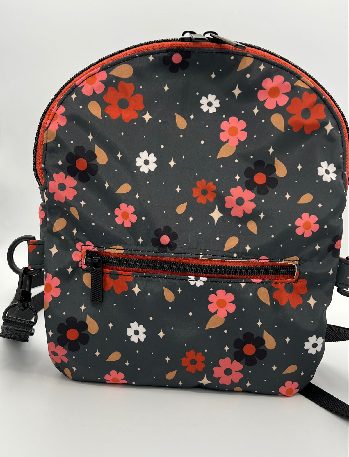 A crossbody bag with a dark gray background and a colorful floral pattern in red, pink, orange, and white. It features a front zippered pocket with a black zipper and a black plastic clip, set against a plain white background.